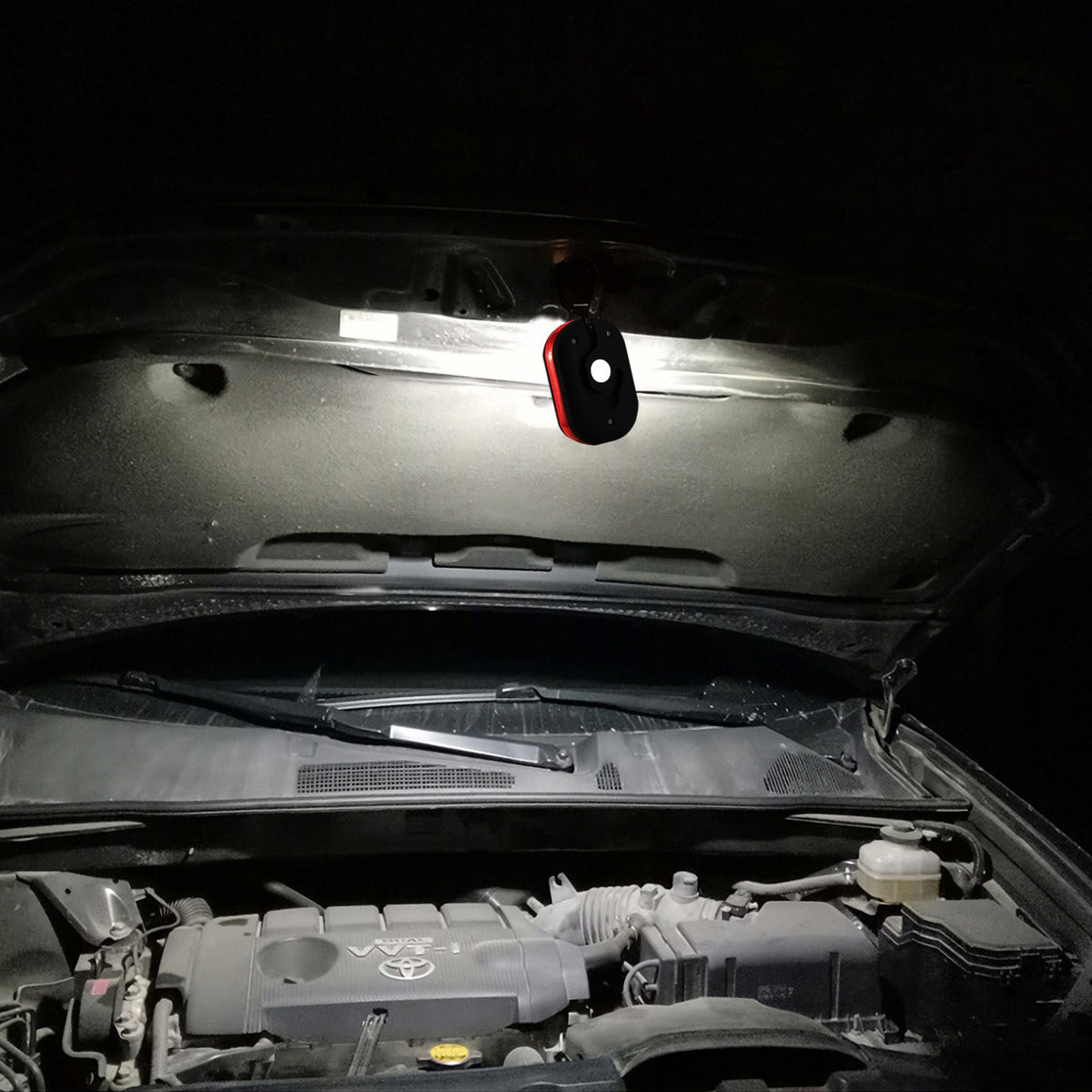 LED work light hanging under a car hood at night